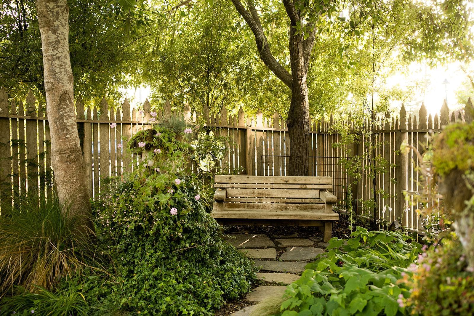 Wooden bench in a garden with a wooden fence, greenery, and a stone pathway.