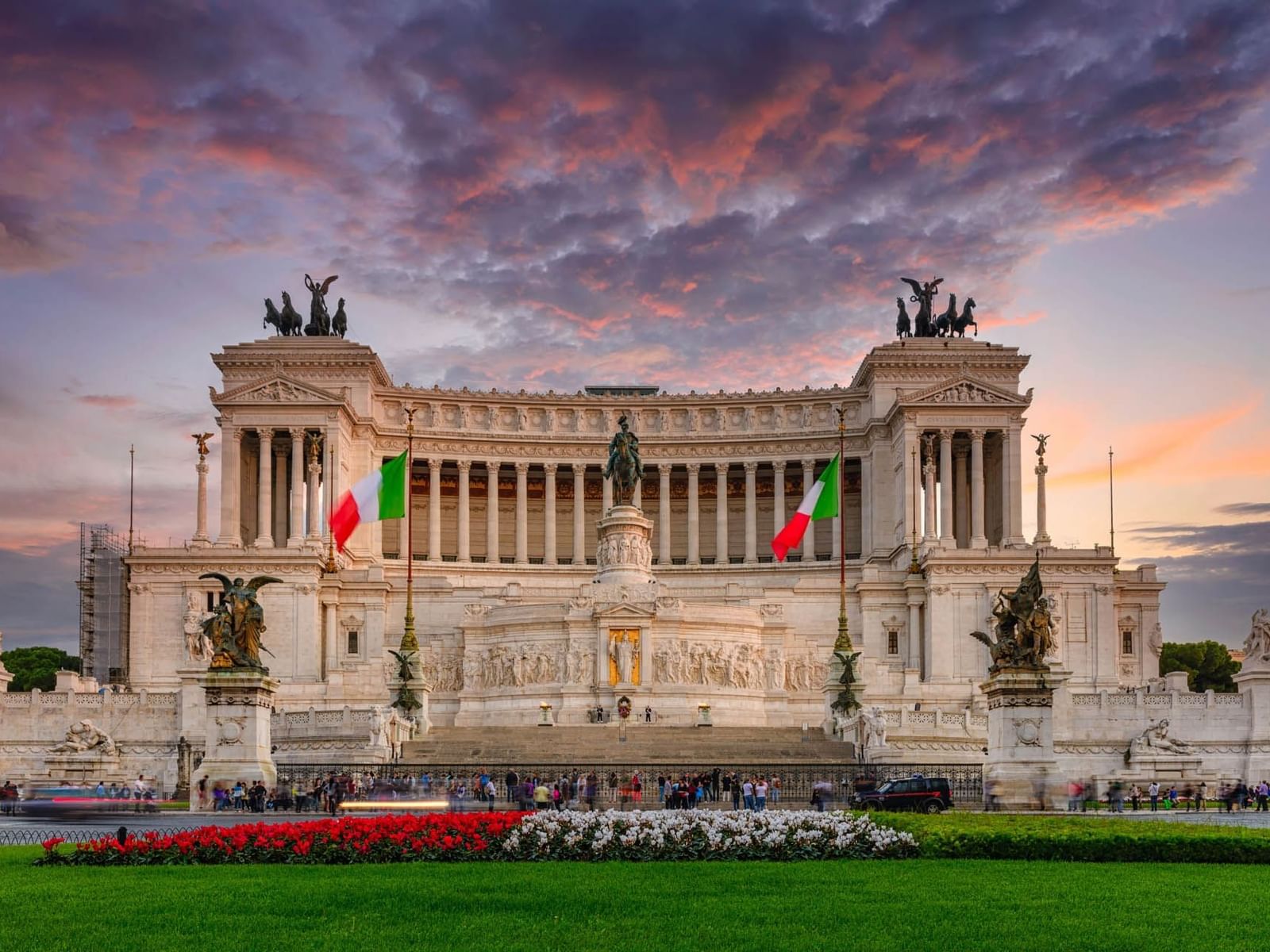 Majestic Altare della Patria at sunset, with Italian flags and vibrant flowers in the foreground near The Guardian Hotel