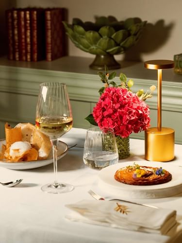 Elegant table setting with gourmet dishes, white wine, and vibrant pink flowers at Le Céladon, Hôtel Westminster - Paris