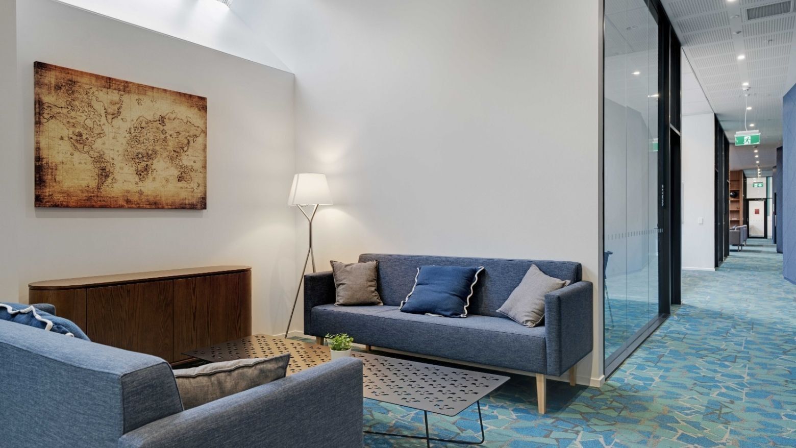 Modern lounge area with blue sofas, world map artwork, and floor lamp at UniLodge Auckland Central
