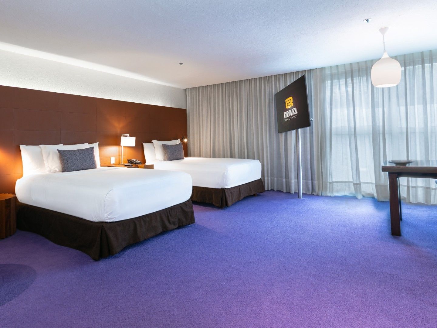 2 Double Junior Suite with twin beds, purple carpet, and a TV on a rotating stand at Camino Real Polanco Mexico