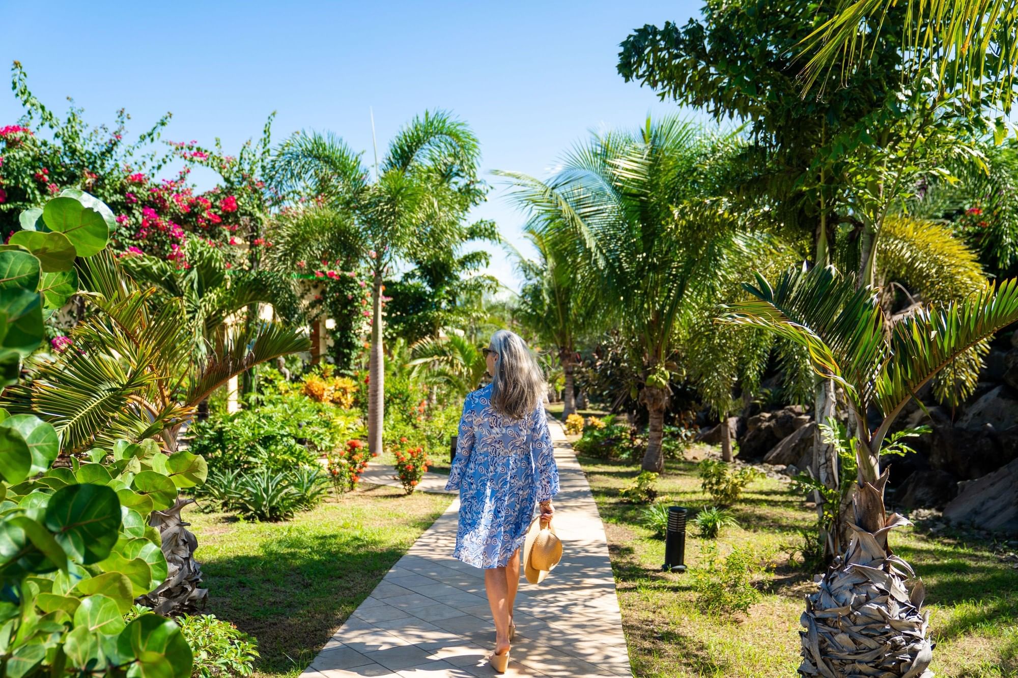 Woman walking along a paved garden pathway surrounded by beautiful tropical palm trees at Golden Rock Resort