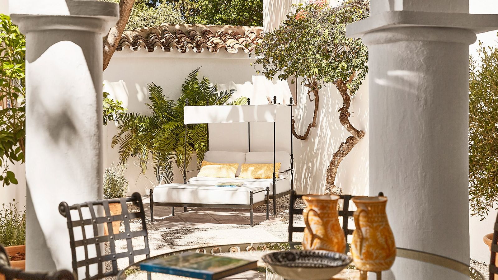 Maria Luisa sunny courtyard with a  canopy daybed, terracotta tile roof, and twisted small tree trunk at Marbella Club