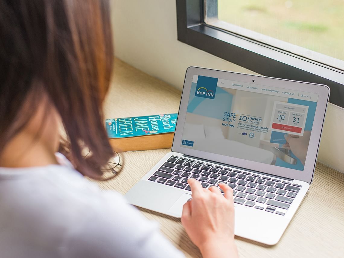 Woman using a laptop with Hop Inn Hotel booking website on screen