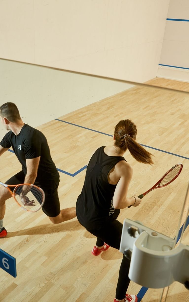 Two guests playing squash with rackets on a wood court marked by blue lines in the fitness club at Hotel X Toronto