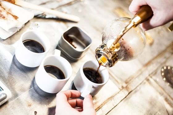Pouring hot coffee into white cups by a silver tray under bright light at The J House Greenwich