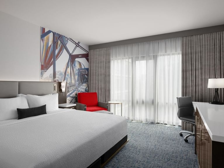 Boutique King room with a king bed, a vibrant red armchair, and an artistic mural of a bridge at Hotel 43 Boise