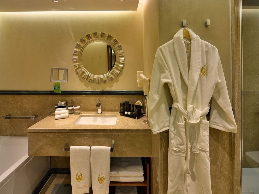 White bathrobe on a hook by a marble vanity under a round sunburst mirror in Ankara Suite with Terrace at Warwick Ankara