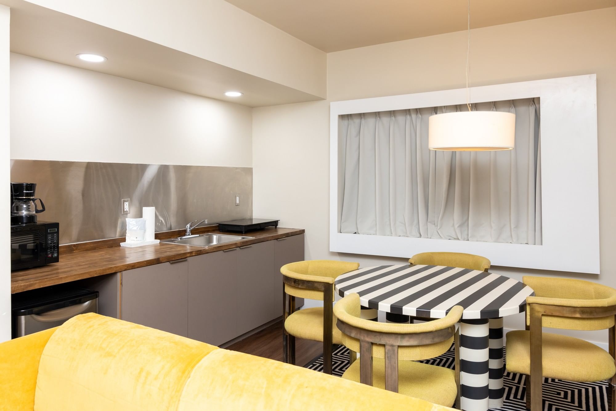 A wide view of a hotel room's kitchenette and dining area with a yellow sofa, table, and chairs.