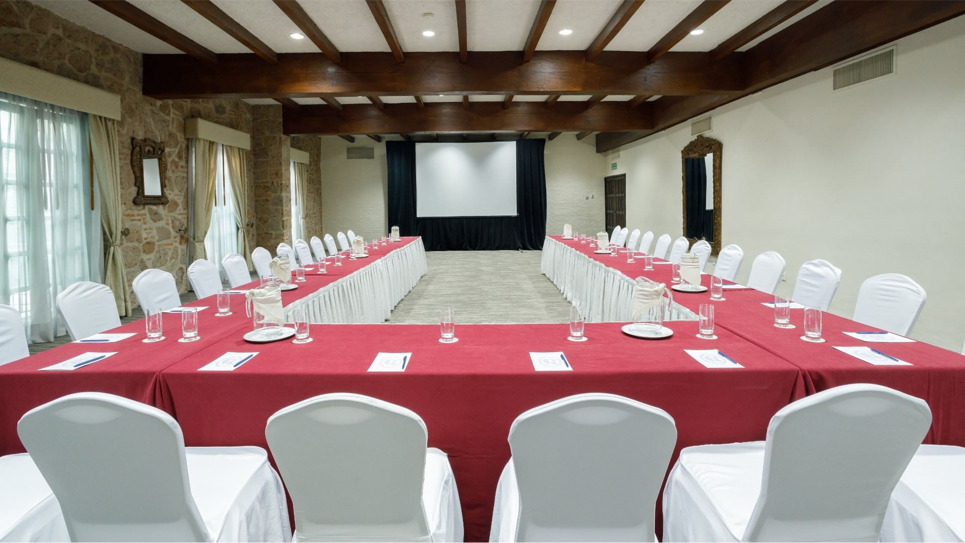 Salón Virreinal with a U-shaped table, red linens, and large screen at Quinta Real Guadalajara