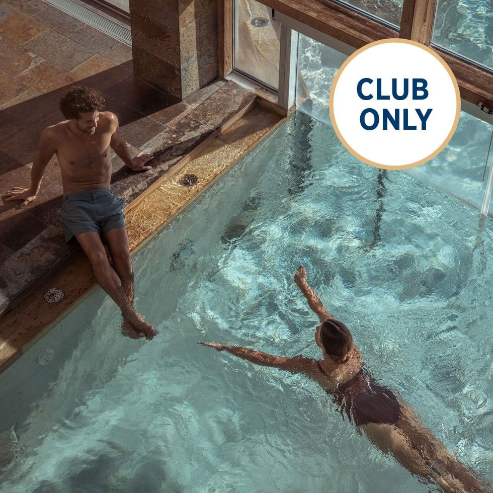 Ein Mann sitzt am Poolrand, während eine Frau im Wasser schwimmt, mit einem 