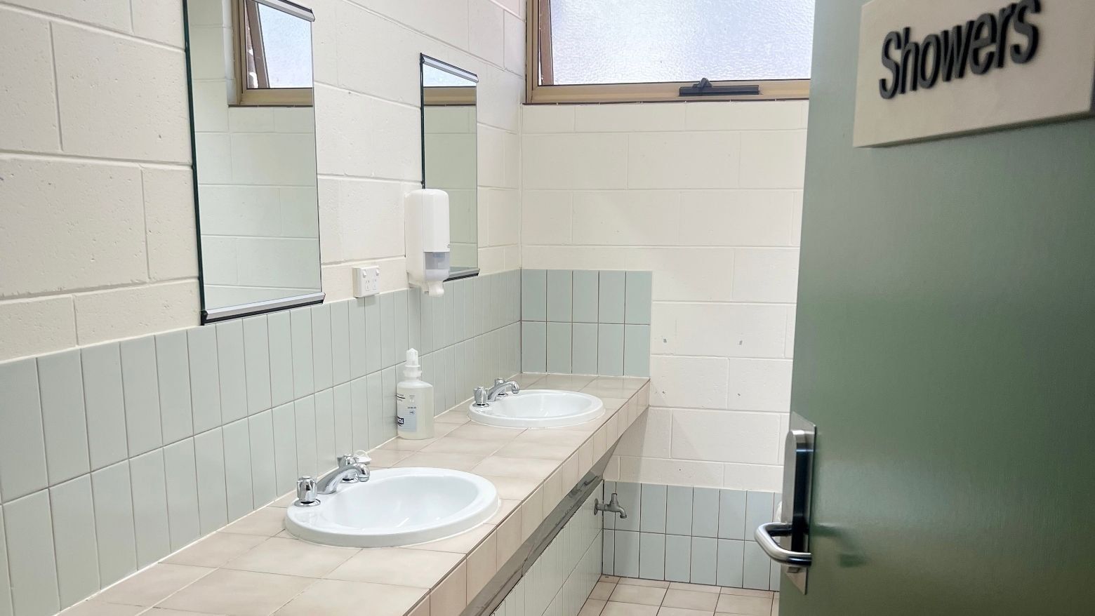 Two sinks with faucets and soap dispenser in a tiled washroom with 