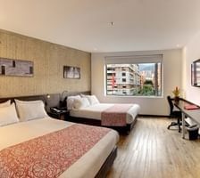 Guest room with two beds, a gray sofa, and a window overlooking the city at Unika Hotels, the best places to stay in Bogota