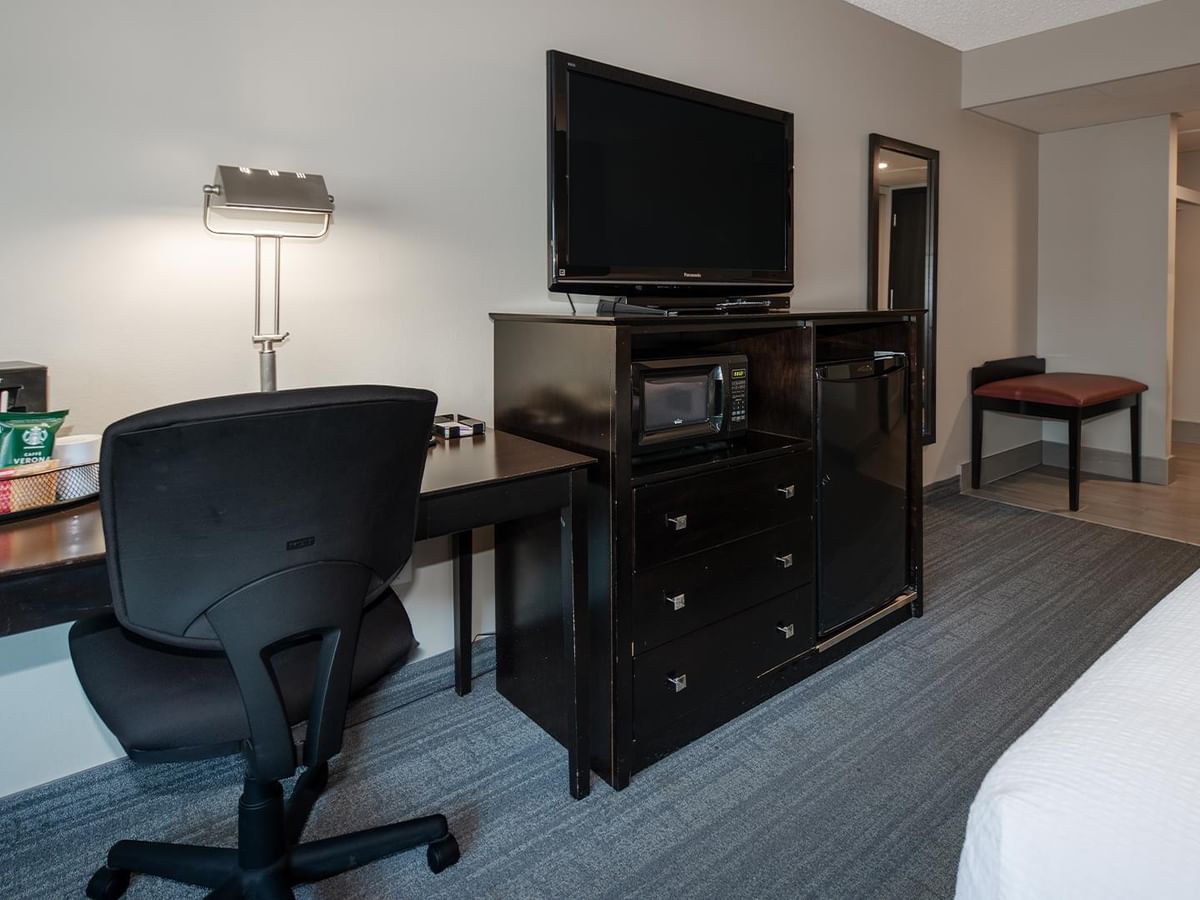 Hotel room with desk, TV, coffee machine, mini fridge and bed.