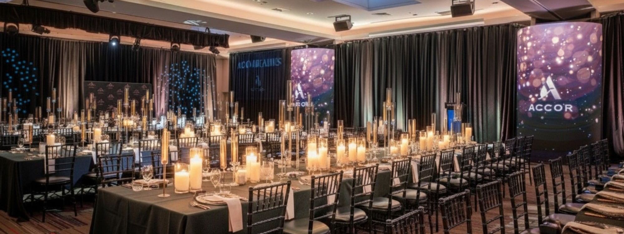 Elegant banquet hall with candlelit tables, dark green linens, and illuminated screens for special events and offers
