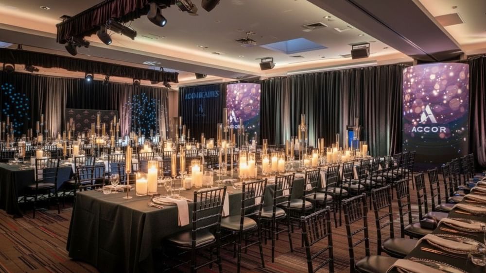 Elegant banquet hall with candlelit tables, dark green linens, and illuminated screens for special events and offers