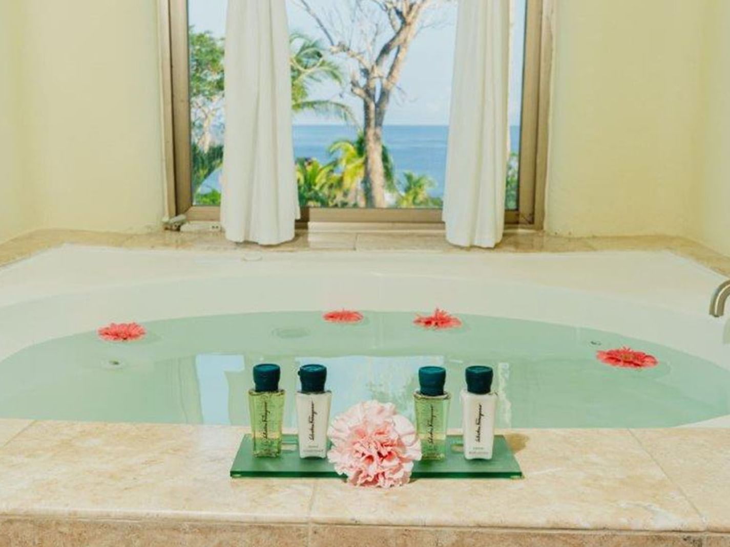 King Grand Class Suite Deep soaking tub with pink flowers and a window view of the Ocean coast at Quinta Real Huatulco