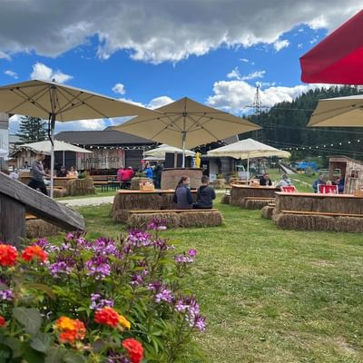 Outdoor seating area with hay bales, umbrellas, and people under a partly cloudy sky.
