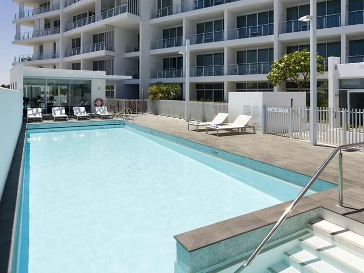Scenic view of outdoor pool with sun loungers and The Sebel Mandurah exterior under a sunny sky