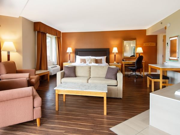 Hotel suite with king bed, sofa, coffee table, work desk, mirror, and a jetted tub