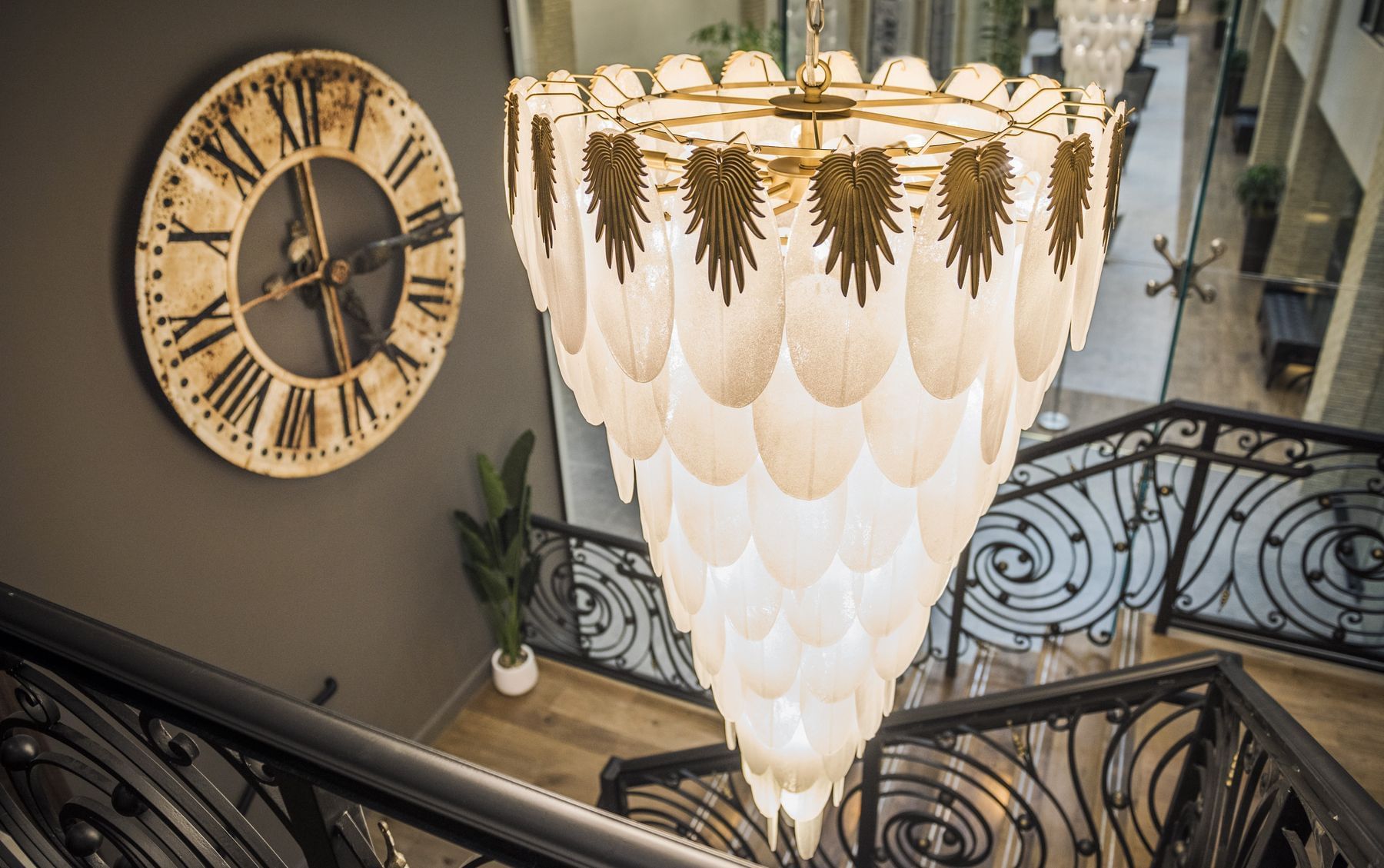 A chandelier hangs from a ceiling above a staircase with a clock on the wall