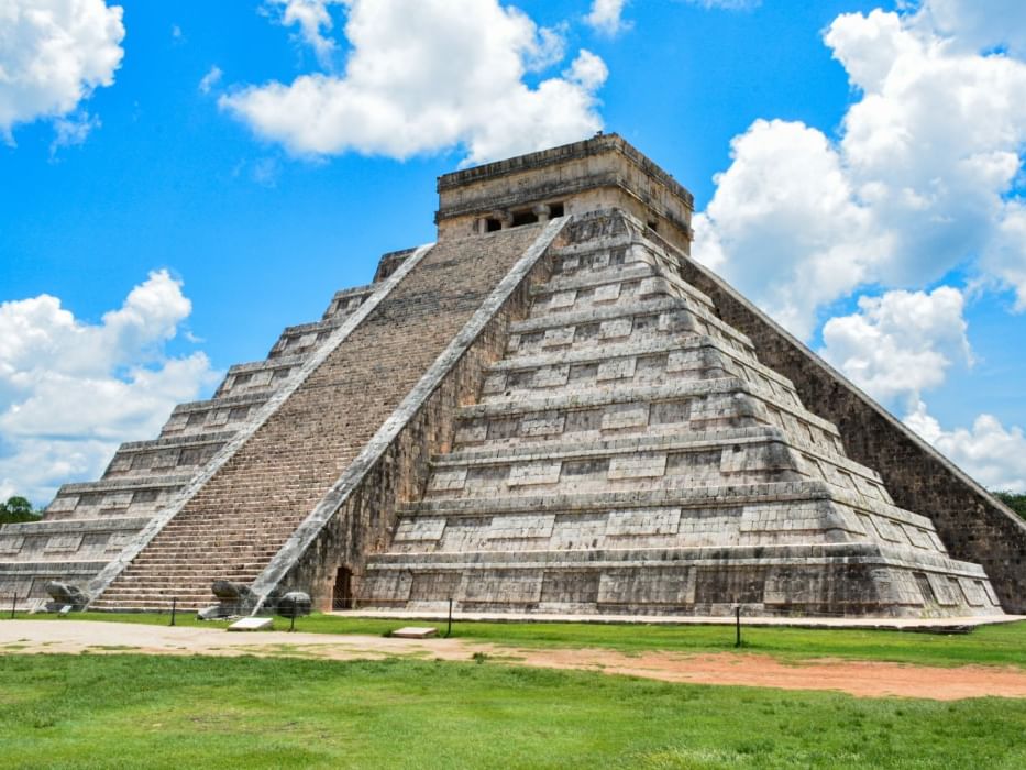Antigua pirámide escalonada de piedra bajo un cielo azul con nubes blancas cerca de Camino Real Hotels