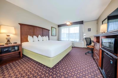 Guestroom with king bed, white linens, work desk, microwave, and mini fridge at Rosen Inn International