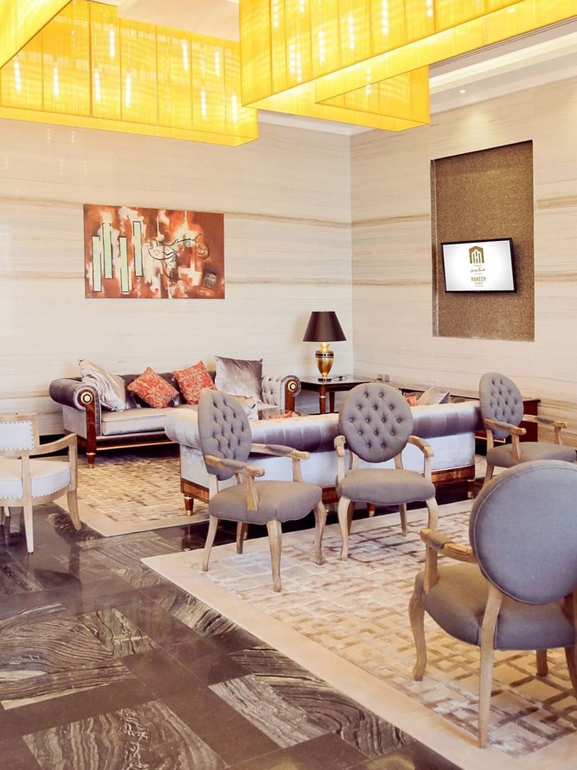 Lobby lounge, featuring grey tufted chairs surrounding rugs under a yellow ceiling at Naviti by Warwick Dammam