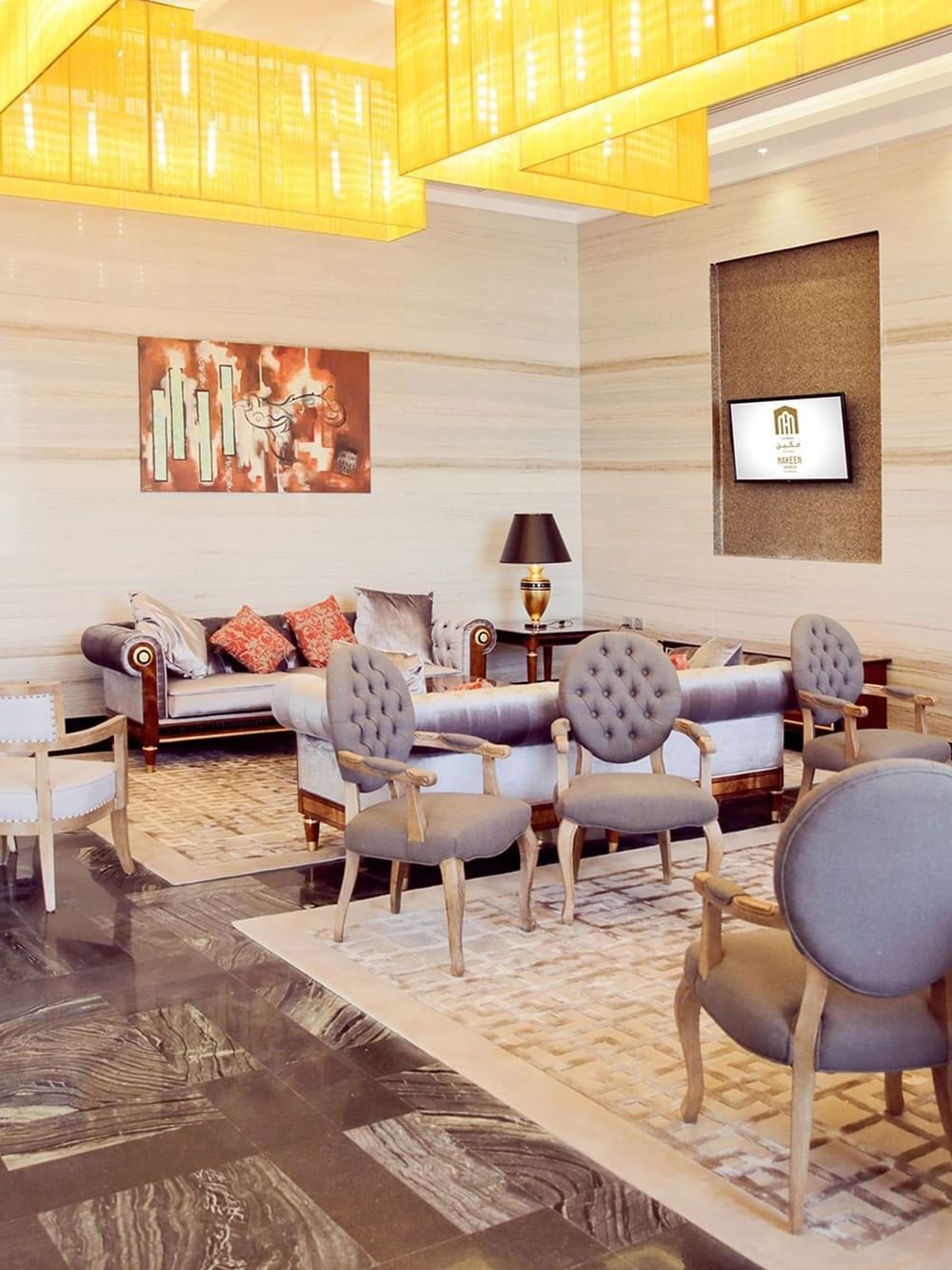 Salon du hall d'entrée, avec des fauteuils capitonnés gris disposés autour de tapis sous un plafond jaune, au Naviti by Warwick Dammam