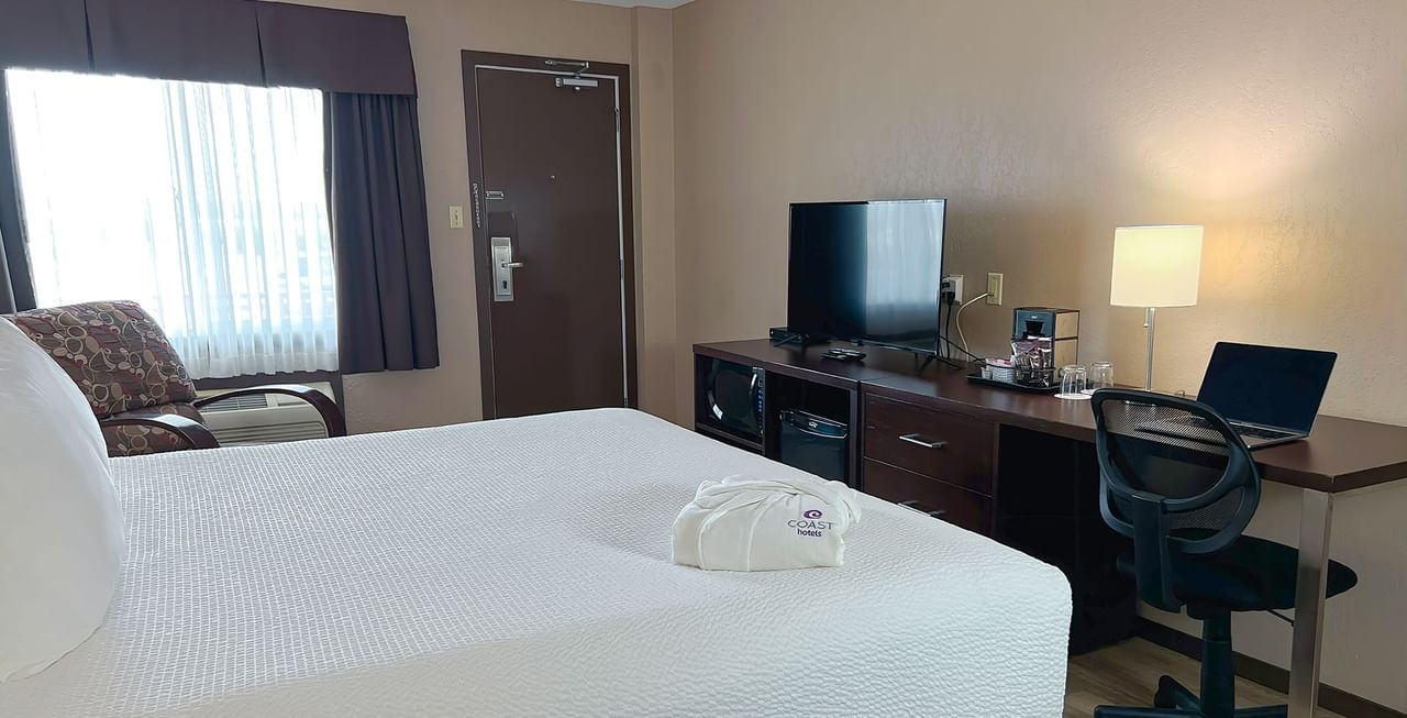Hotel bedroom with bed, TV, table, chair, and bath robe