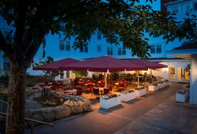 An outdoor patio at night in Cascades Restaurant at The Stanley Hotel, with tables and chairs under red umbrellas