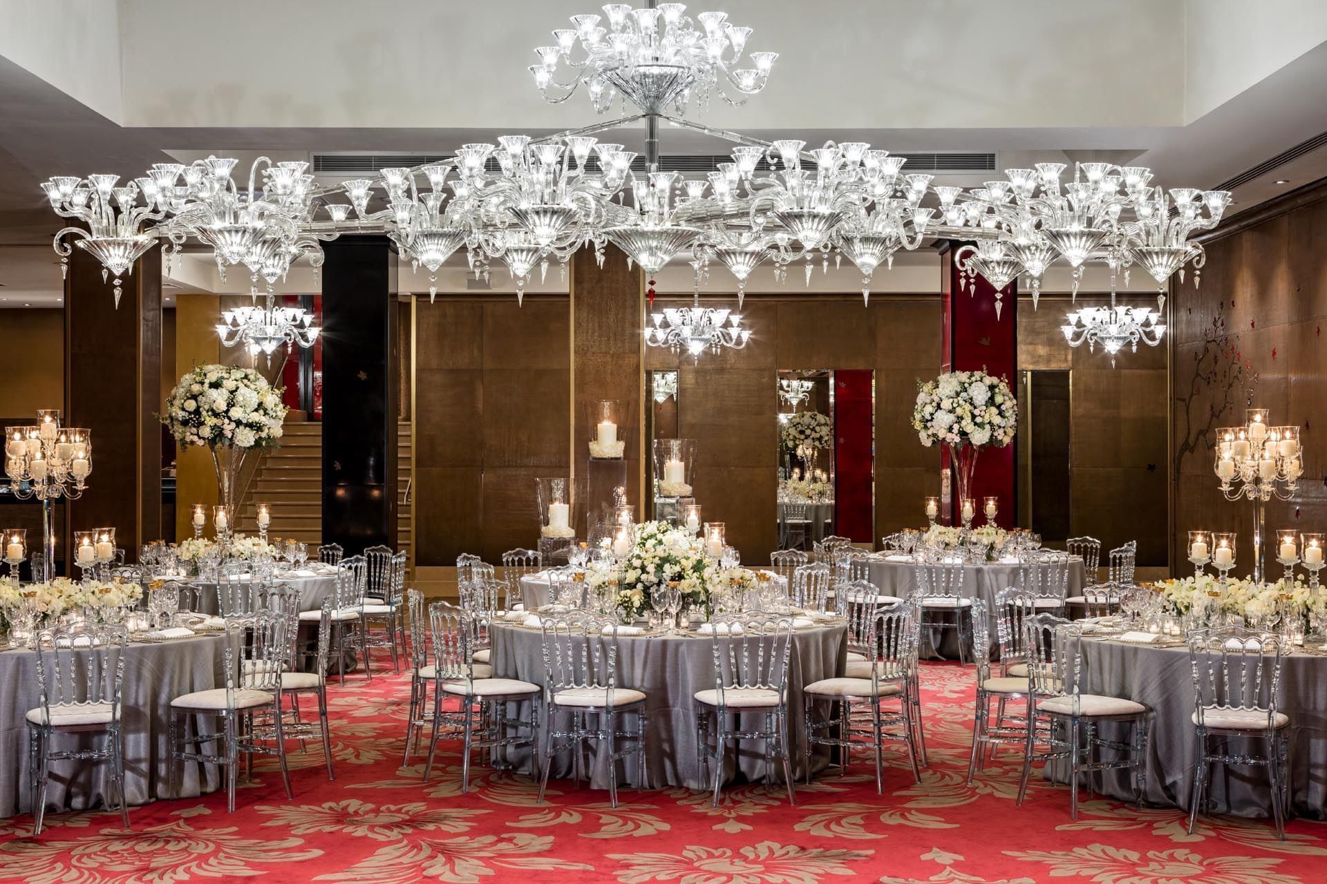 Wedding reception featuring elegant round tables with floral centerpieces under sparkling chandeliers at The May Fair Hotel