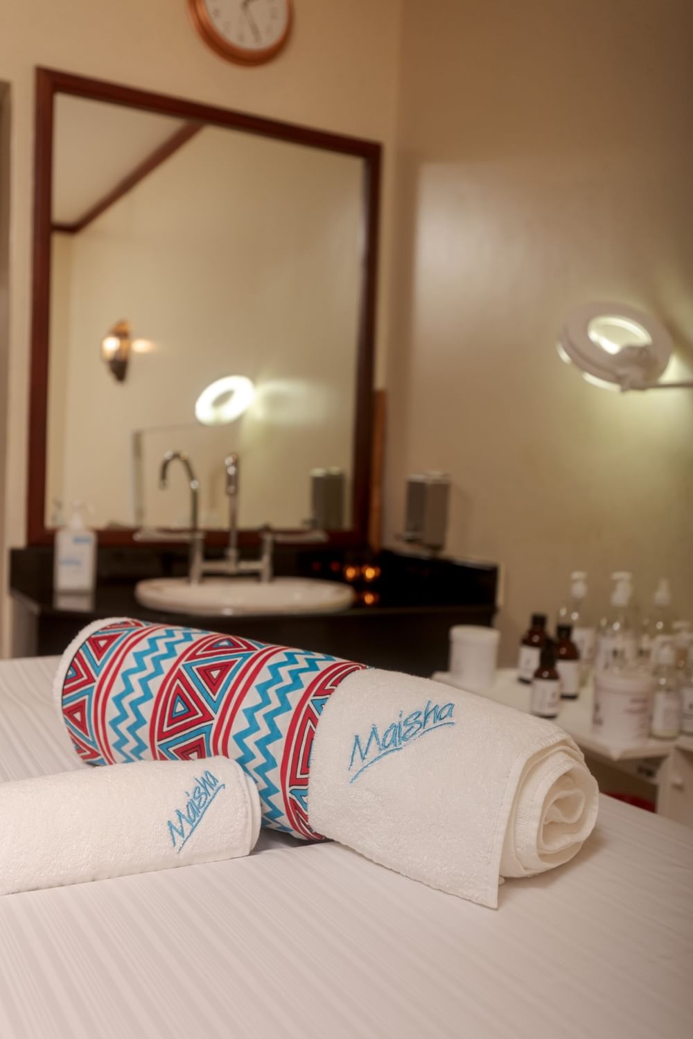 Rolled Maisha towels on a white massage bed in a spa treatment room by a framed mirror at Kampala Serena Hotel