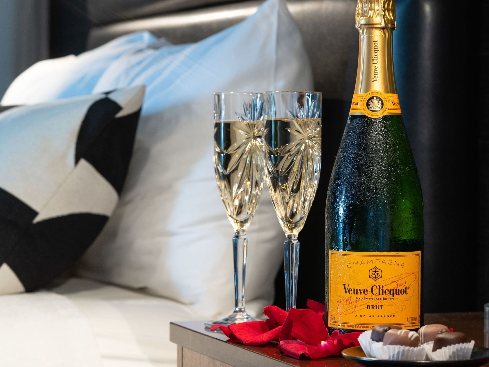 Bottle of Veuve Clicquot and rose petels beside the bed