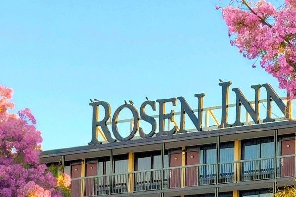 A close-up of the sign reading Rosen Inn on top of the hotel surrounded by beautiful pink flowers.