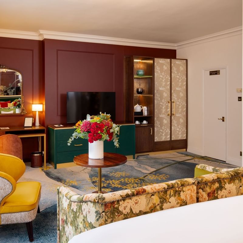 Elegant room with floral couch, yellow chair, TV, and vibrant floral arrangement in the heart of Knightsbridge.