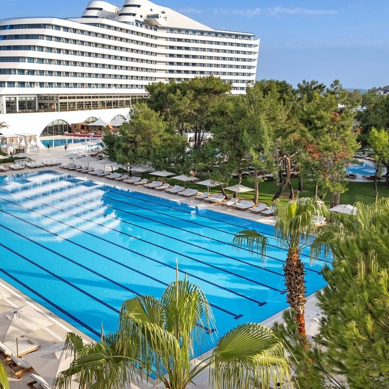 Güneşli bir günde Titanic Deluxe Lara’nın Olimpik havuzuna yukarıdan bakış; geniş yüzme alanı ve lüks tatil atmosferiyle dikkat çekiyor.