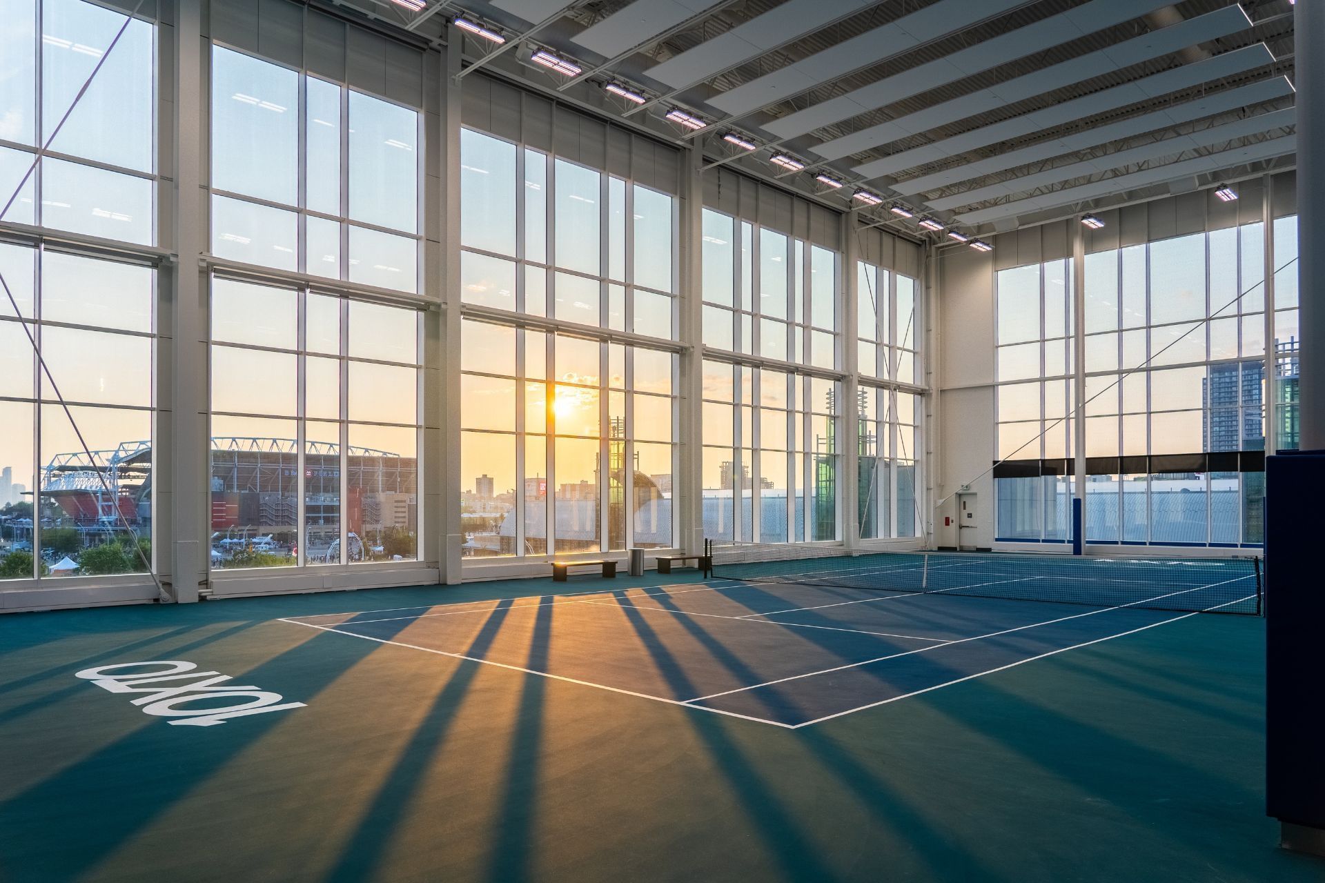 Indoor tennis court with large windows and sunset over the city skyline