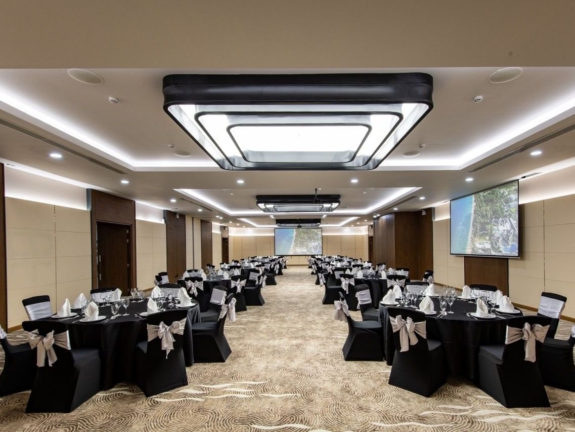 The Galaxy Room with black round tables, dual projection screens and white ribbon accents at Amora Beach Resort Phuket,