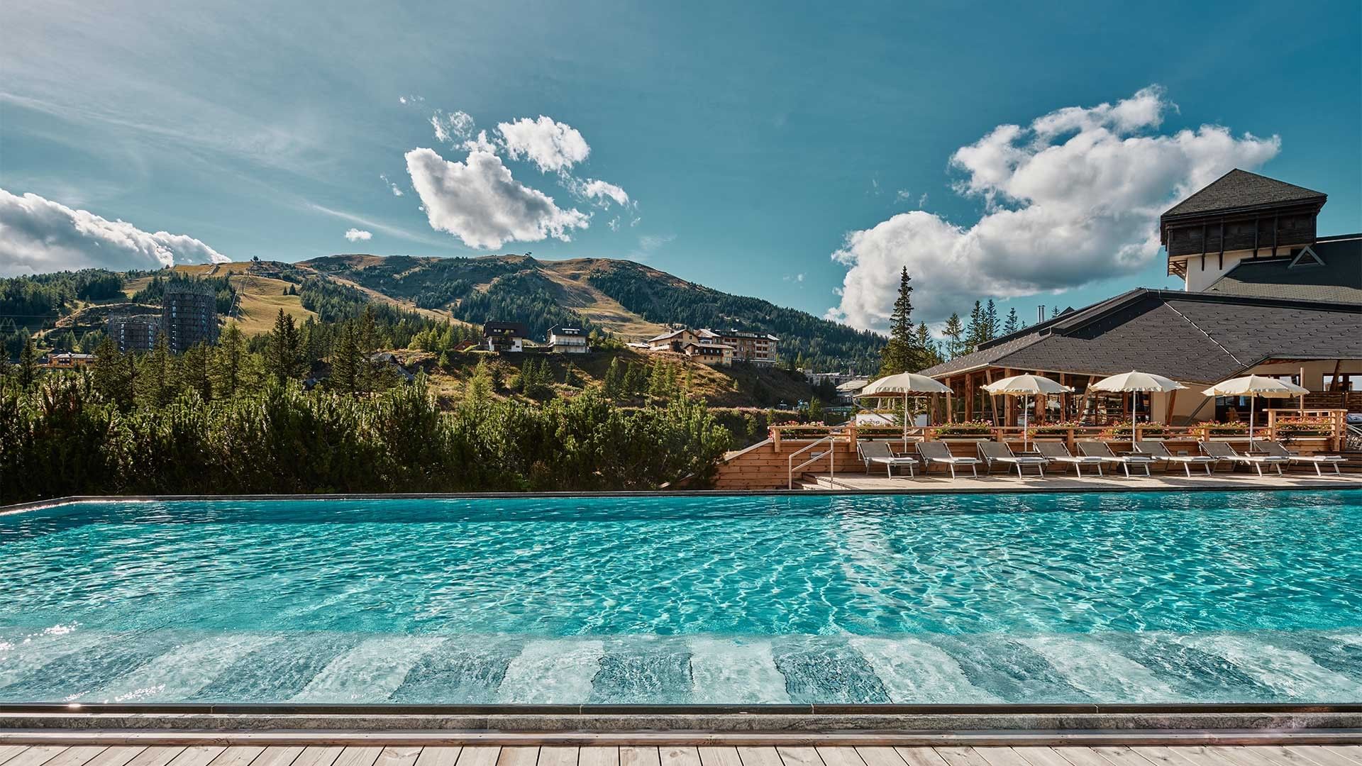 Large pool with lounge chairs and umbrellas, set against a mountain backdrop.