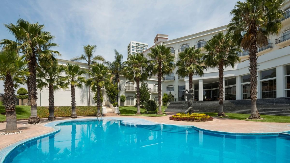 Piscina exterior de lujo rodeada de altas palmeras y habitaciones del hotel en Camino Real Puebla Angelopolis