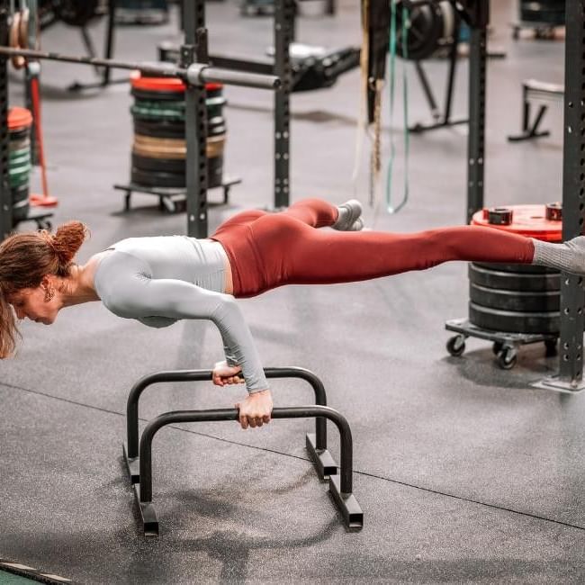 Woman doing an elbow lever on parallel bars in a gym illustrating the benefits of calisthenics.