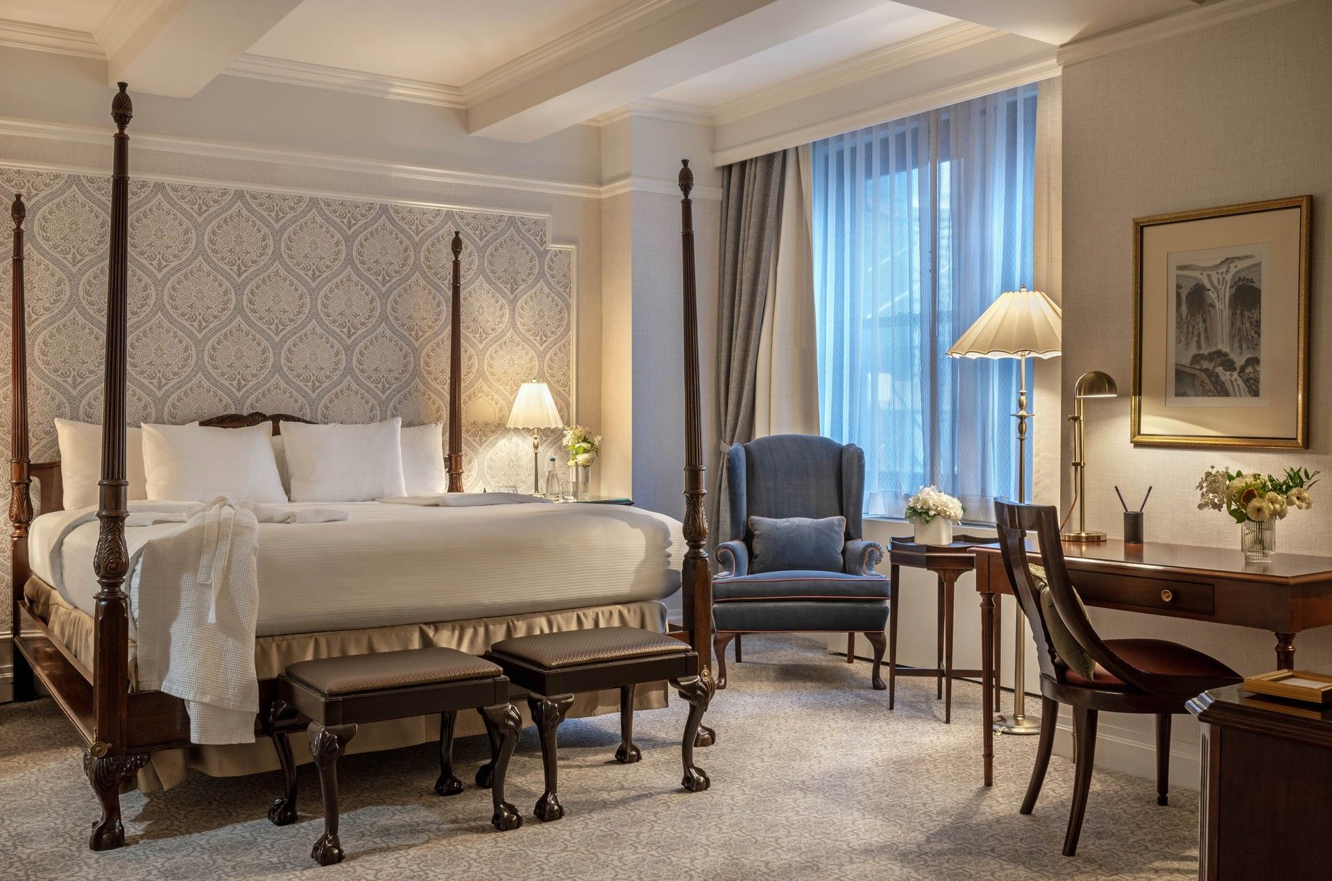 Four-poster bed with damask wallpaper, and a cozy blue wingback chair in Suites of the Stars at Warwick New York 