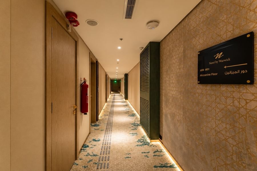 Hotel corridor with patterned carpet beside Mezzanine Floor directional sign on elegant wall at Naviti by Warwick Jeddah