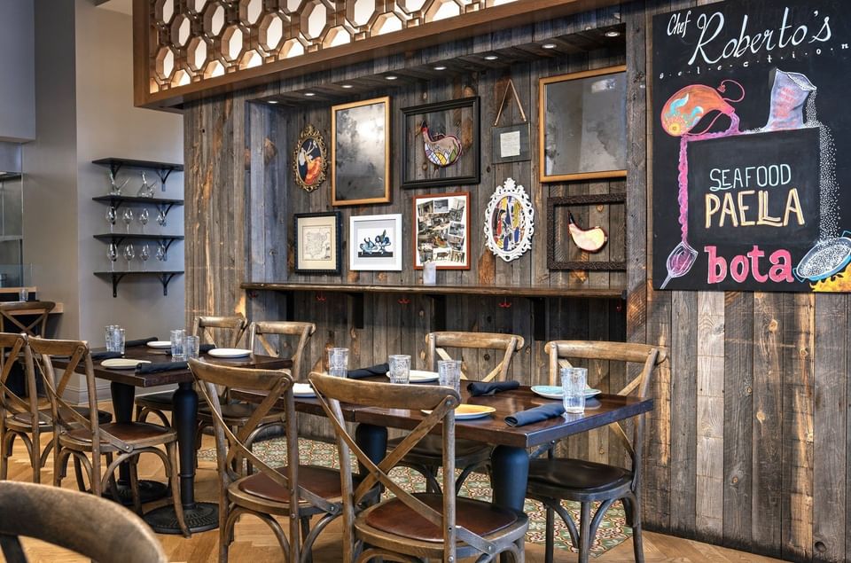 Wooden chairs by dark tables under a rustic wall with framed art in BOTA at Warwick San Francisco