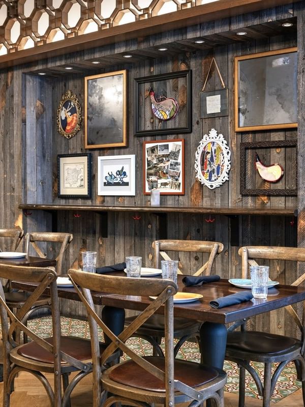 Wooden chairs by dark tables under a rustic wall with framed art in BOTA at Warwick San Francisco