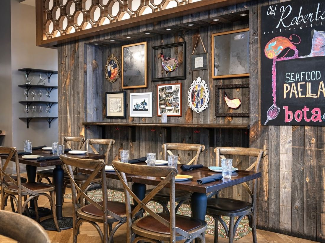 Wooden chairs by dark tables under a rustic wall with framed art in BOTA at Warwick San Francisco