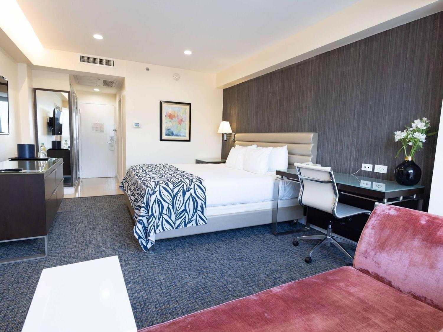 Plush bed and work desk beside pink velvet sofa seating area in Deluxe One Bedroom King Suite at Jamaica Pegasus Hotel