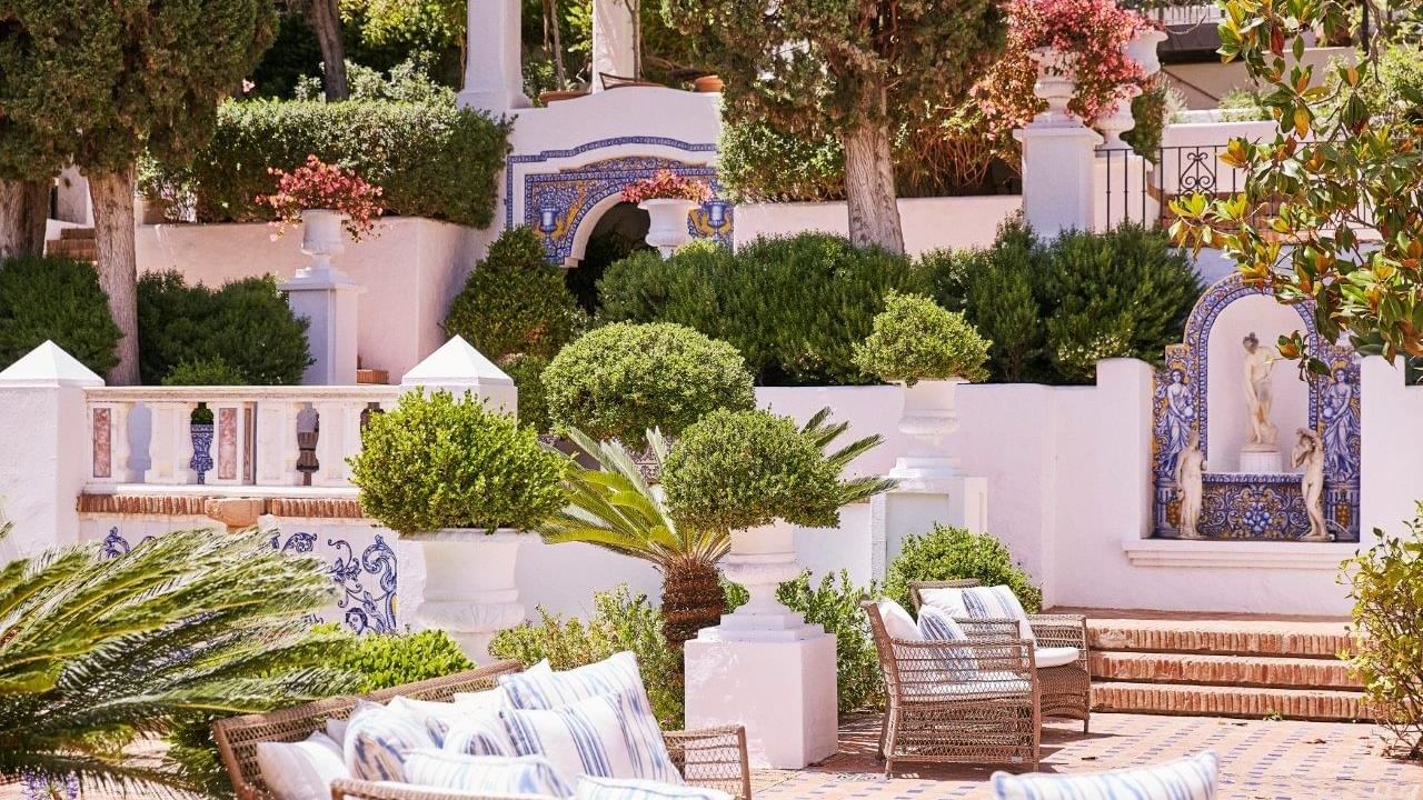 Villa del Mar garden terrace with white stucco walls, blue mosaic tile accents, & wicker seating at Marbella Club