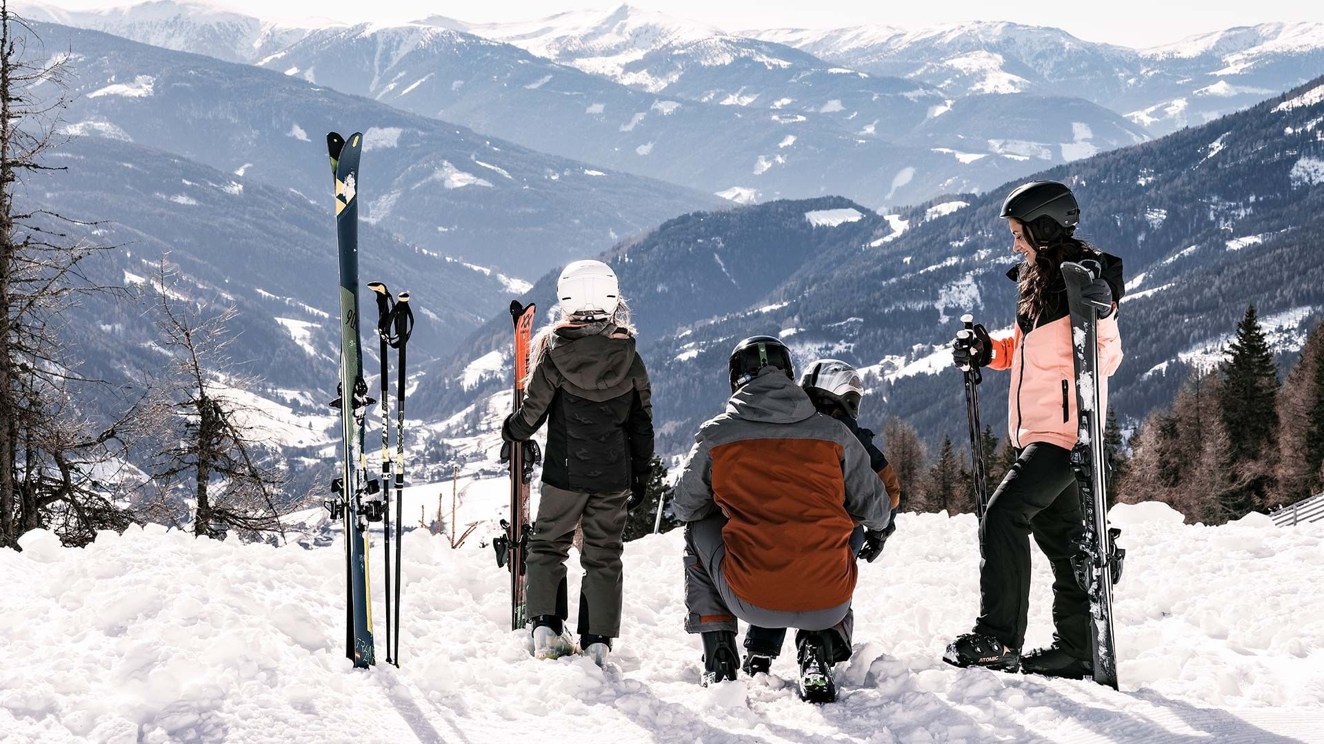 Četvero skijaša u zimskoj odjeći i s kacigama stoji na snijegu s pogledom na planine.